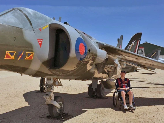 Alex Spartz, an engineering student and wheelchair user, sits in front of an airplane at the Pima Air and Space Museum.