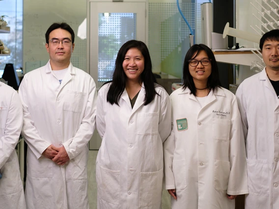 Five people in white lab coats pose for a photo in a lab.