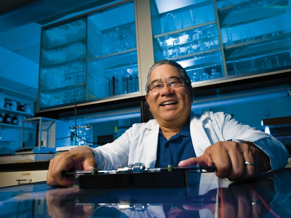 Terry Matsunaga in a laboratory lit with blue light, wearing a lab coat and smiling.