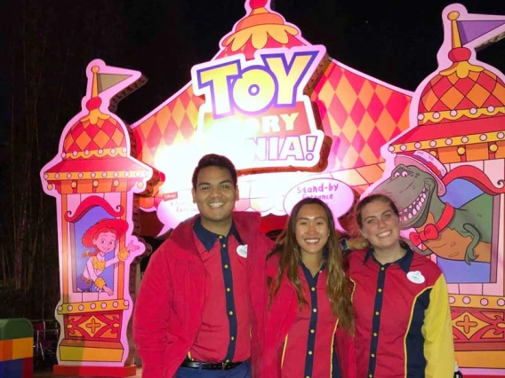 Three smiling people in Disney uniforms in front of the Toy Story Mania! attraction.