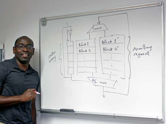 Tosiron Adegbija stands at a whiteboard with a diagram of computer memory caching written on it in black marker