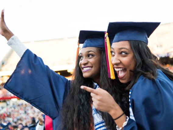 Two women wearing caps and gowns pose for a photo at graduation.
