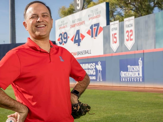 Ricardo Valerdi stands with a baseball and catcher's mitt in a baseball stadium