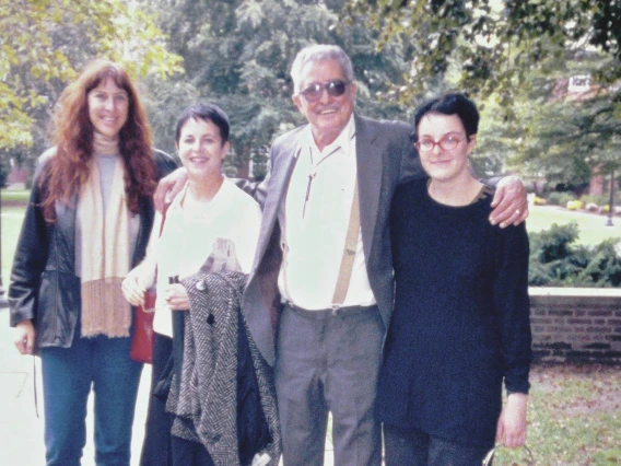 Four people (three women and one man) standing and smiling on a college campus.