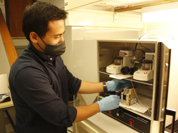 Suchol Savagatrup, wearing a face masks and blue latex gloves, reaches into a cabinet in his lab.