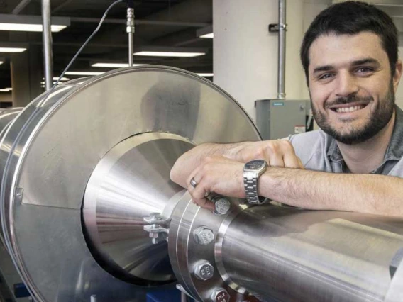 Alex Craig smiles and rests his arm on a 104-foot silver wind tunnel