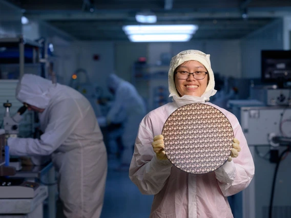 A student in a gown holds a test wafer in the clean room