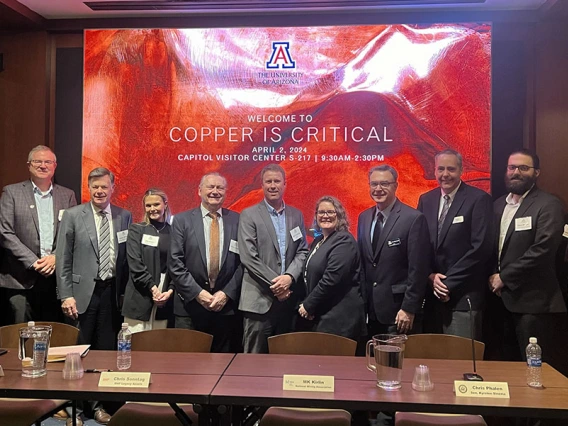 a large group of panelists poses in a conference setting