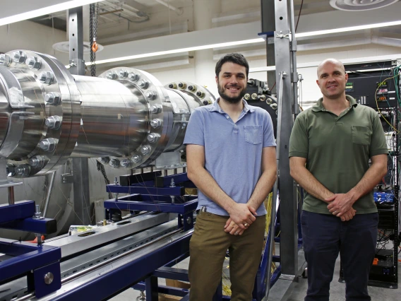 Alex Craig and Jesse Little stand next to a large metal wind tunnel.