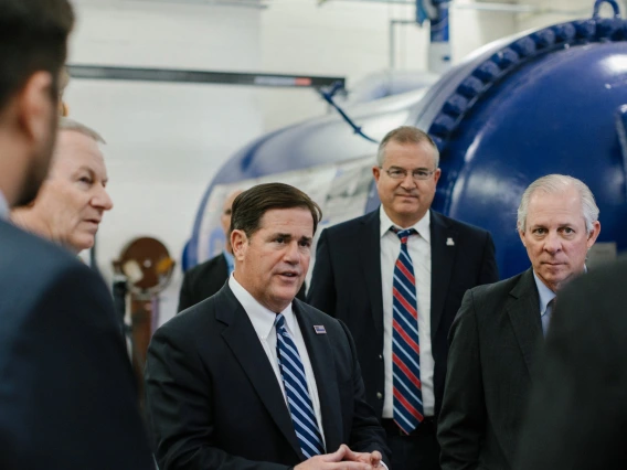 Six men stand next to a blue wind tunnel talking.