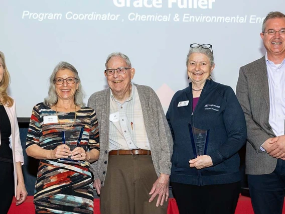 Five people pose with two award statues