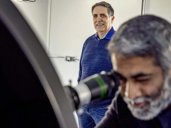 a scientist uses an optical instrument while another stands by