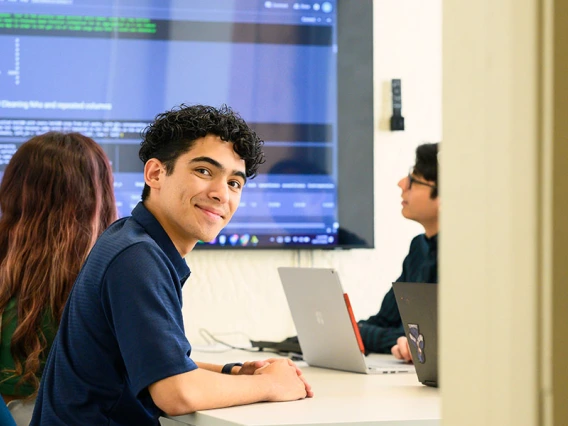 a group of students in a classroom looking at a large monitor