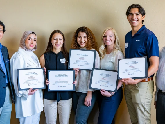 A group of seven people -- five students holding certificates flanked by two professors -- pose for a photo