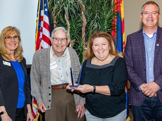 An employee poses for an award with three presenters