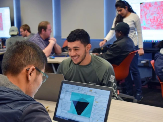 A students, seen from behind, looking at a rending of a mine plan on his laptop. He is in a classroom, and other students can be seen in the background.