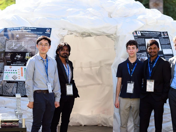 Students stand in front of the tall sandbag structure outdoors