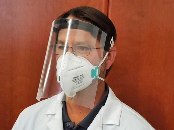 Man wearing a plastic face shield and a white lab coat