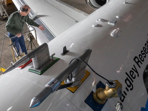 A photo shot from above of a man at the top of a ladder next to a large white airplane, which says "Langley Research Center" on the side.