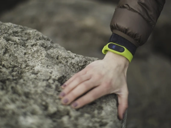 A close-up of a hand resting on a rock. There is a green smartwatch on the wrist.