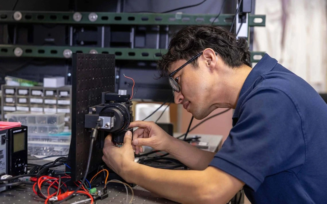 A man in blue shirt looks a microscope.
