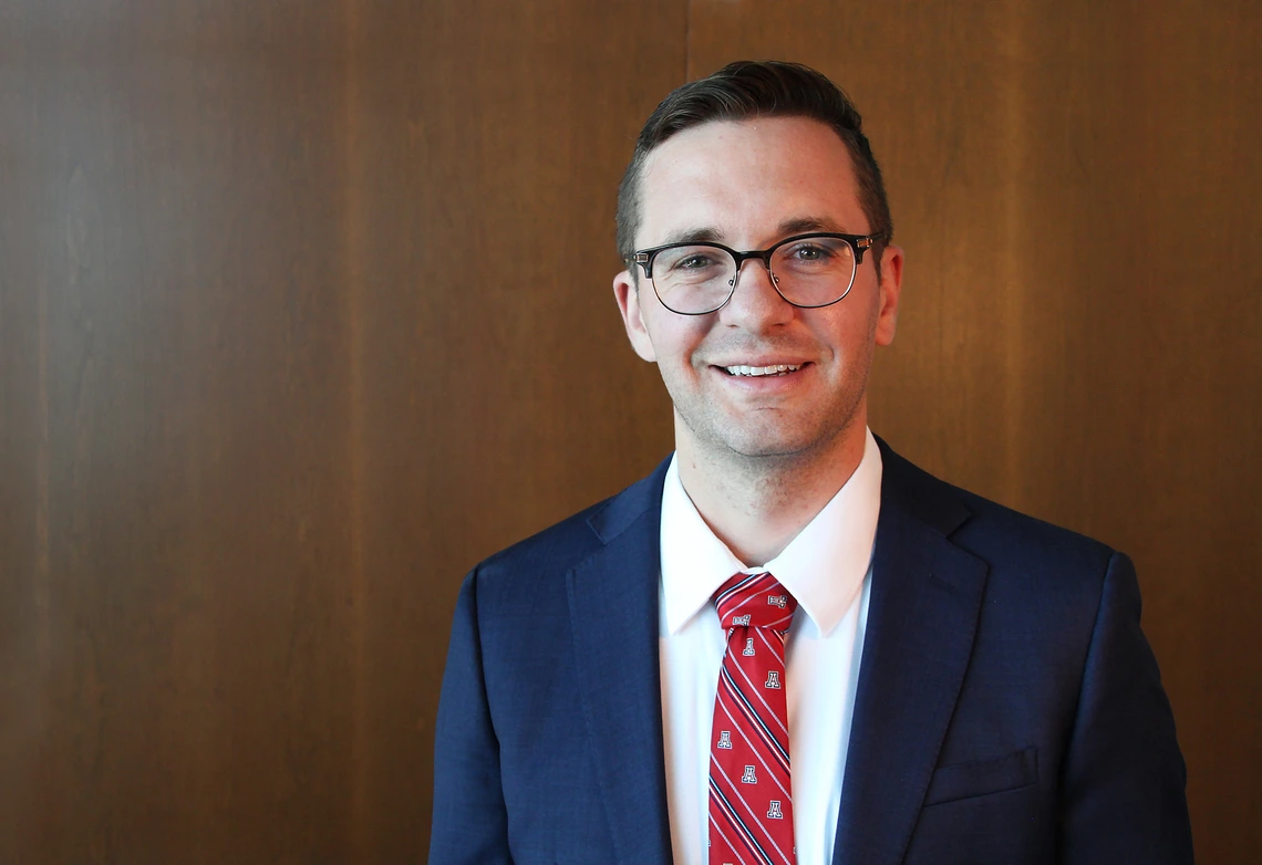 A man with brown hair poses for a photo in a blue blazer.