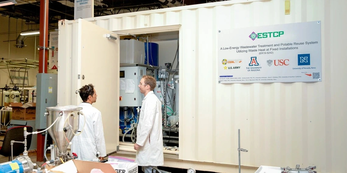 Two men in lab coats stand in front of a large metal shipping container.