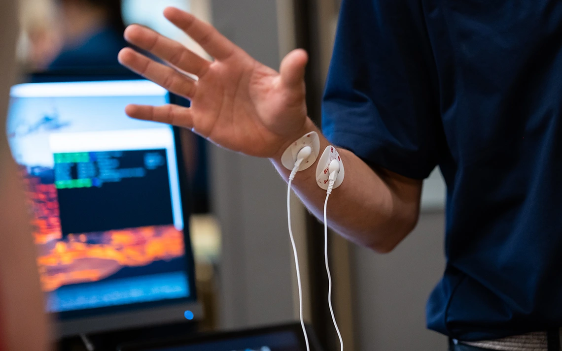 A man in a blue polo demonstrates a medical device on his wrist.