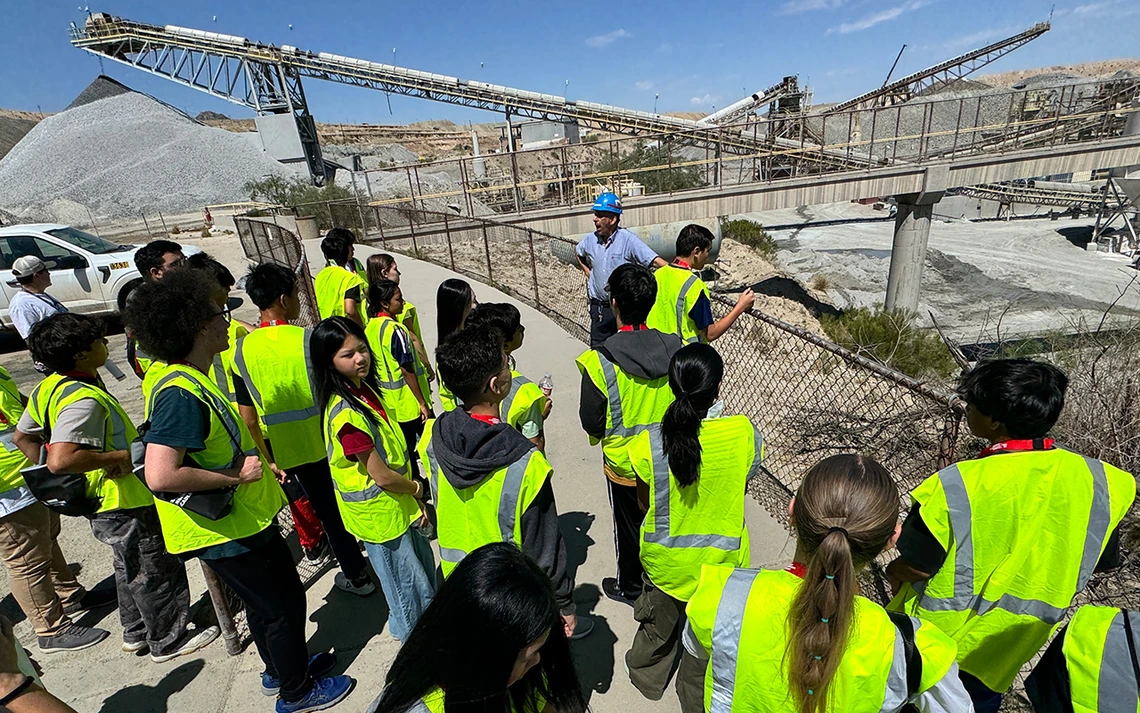 A group of students in yellow vests look over a railing at an open mine pit.