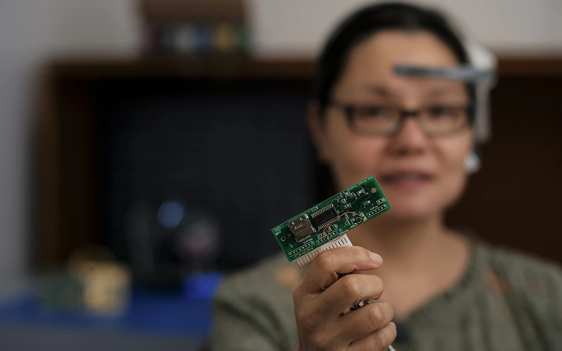 A woman with dark brown hair holds up a computer chip.