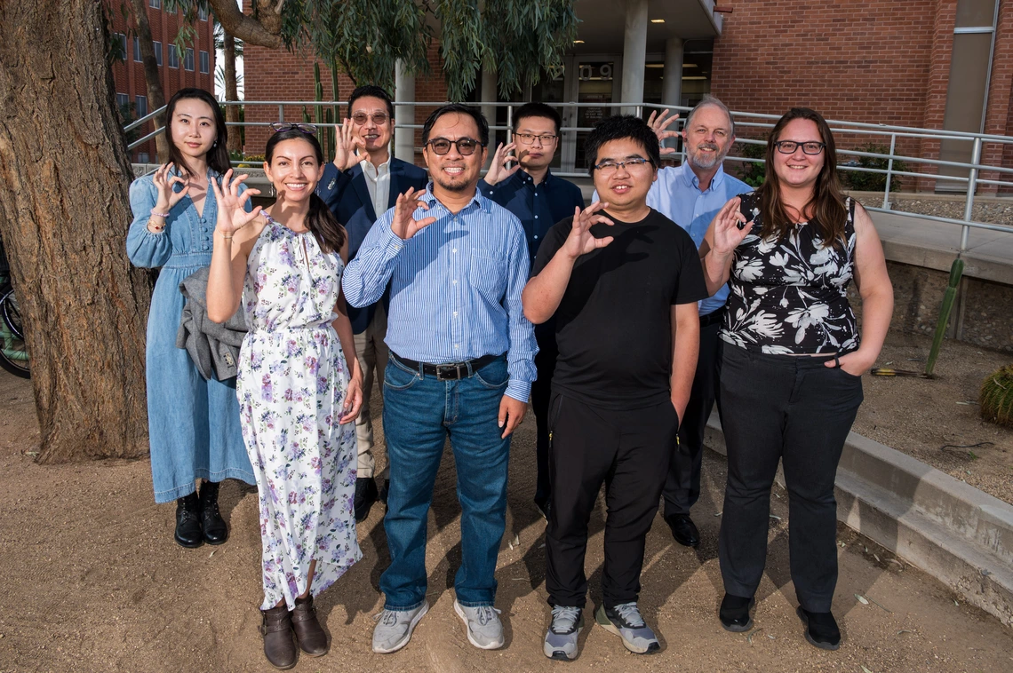 Eight people pose for a photo with hands raised to signify U of A college sign.