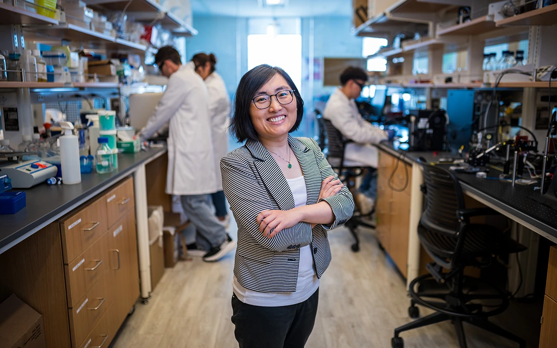 A woman in a grey jacket poses for a photo in a lab.