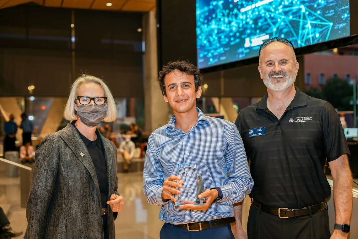 A woman and two men smile for a photo. Sahand Sabet, center, holds a glass award.