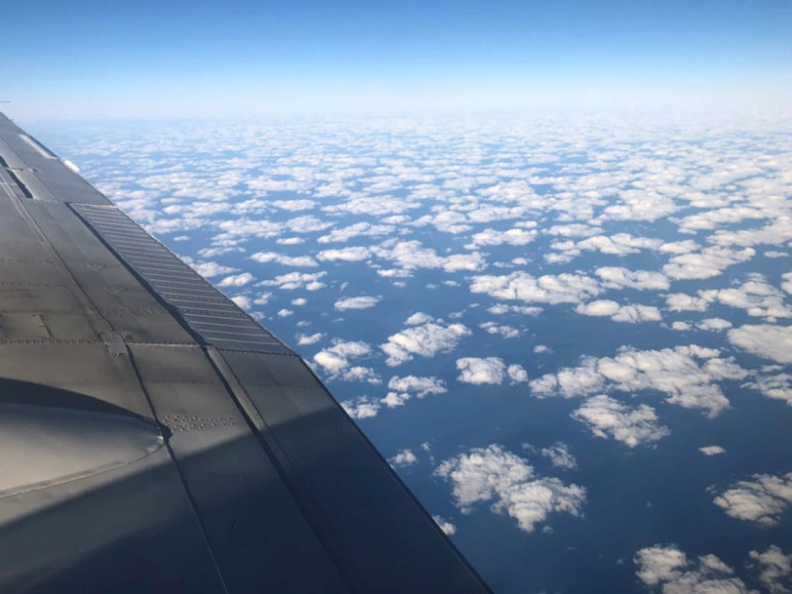 photo taken from a plane showing cumulus clouds from above. The wing of the plane is visible in the left of the frame