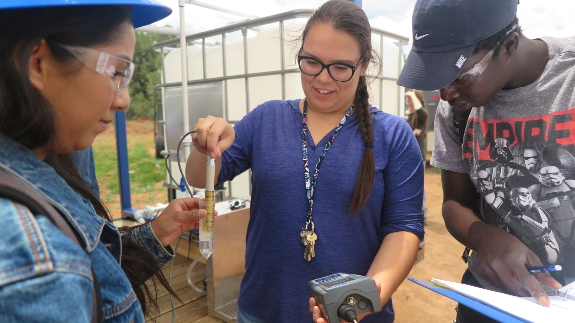 A woman, center, holds a device into a vial of water, while people on either side of her watch.