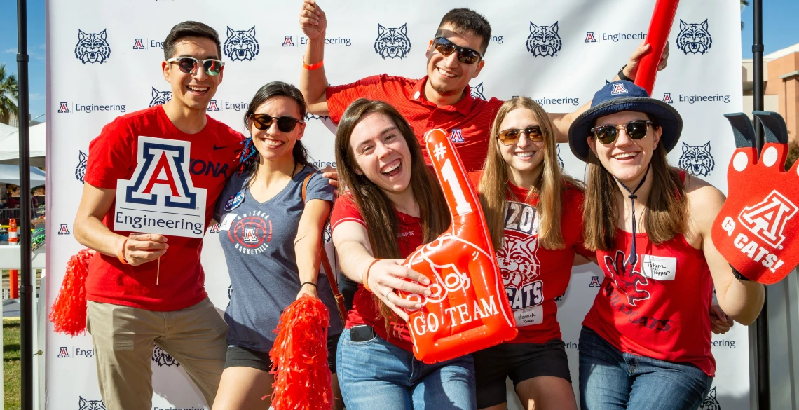 A group of people in Arizona Wildcats gear holding up an inflated #1 finger, pom poms and a UArizona Engineering logo