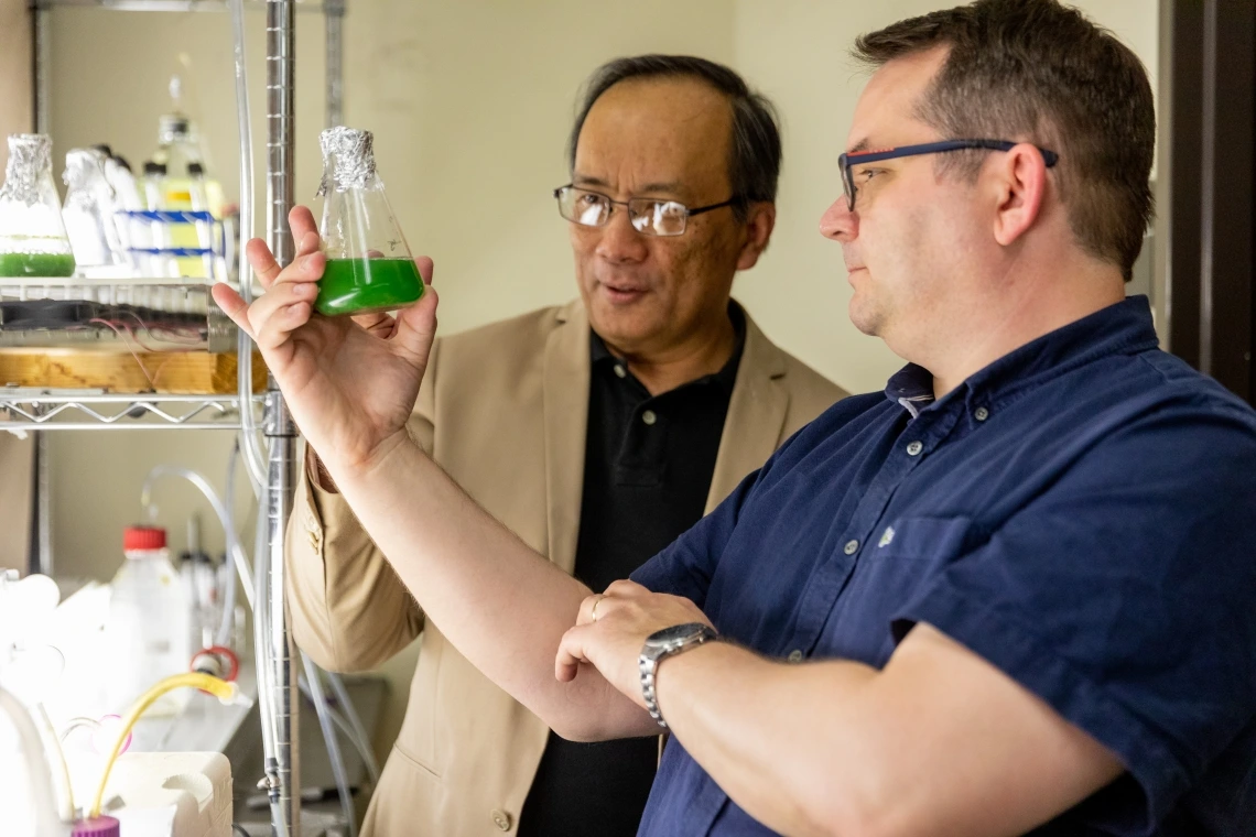 Two men examine a beaker of algae.