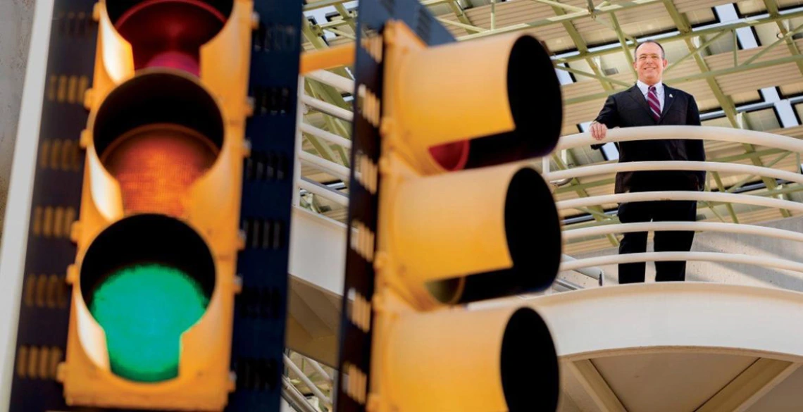 Larry Head is wearing a suit posing behind a traffic signal light