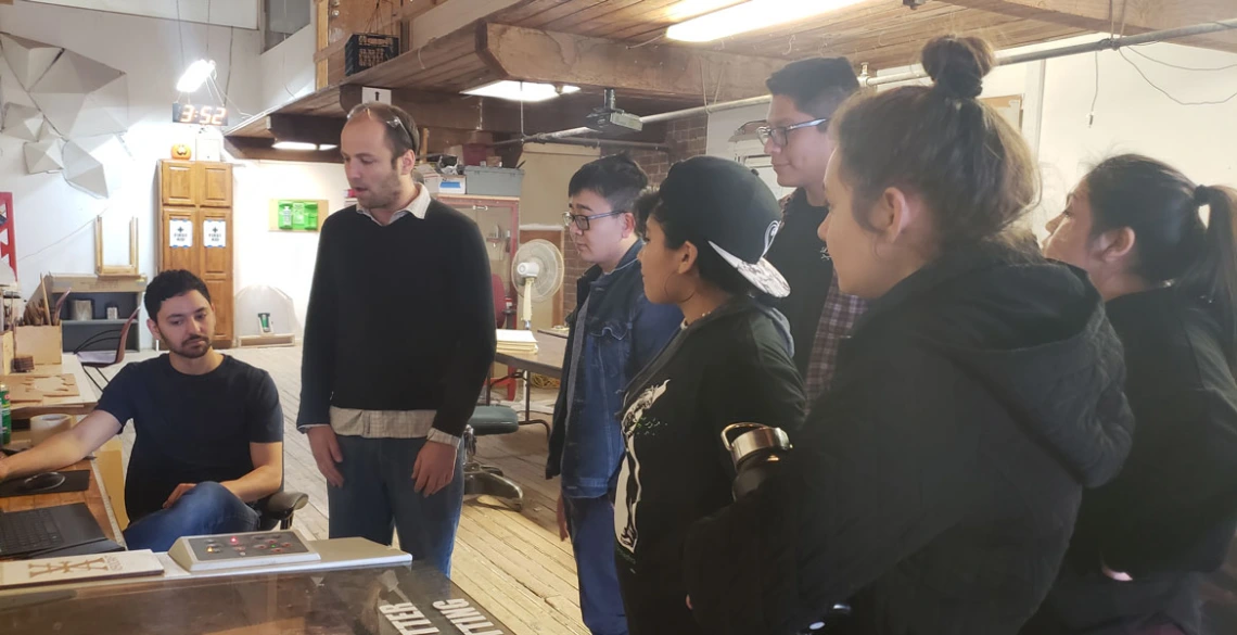 A group of students gather around to watch a demonstration.