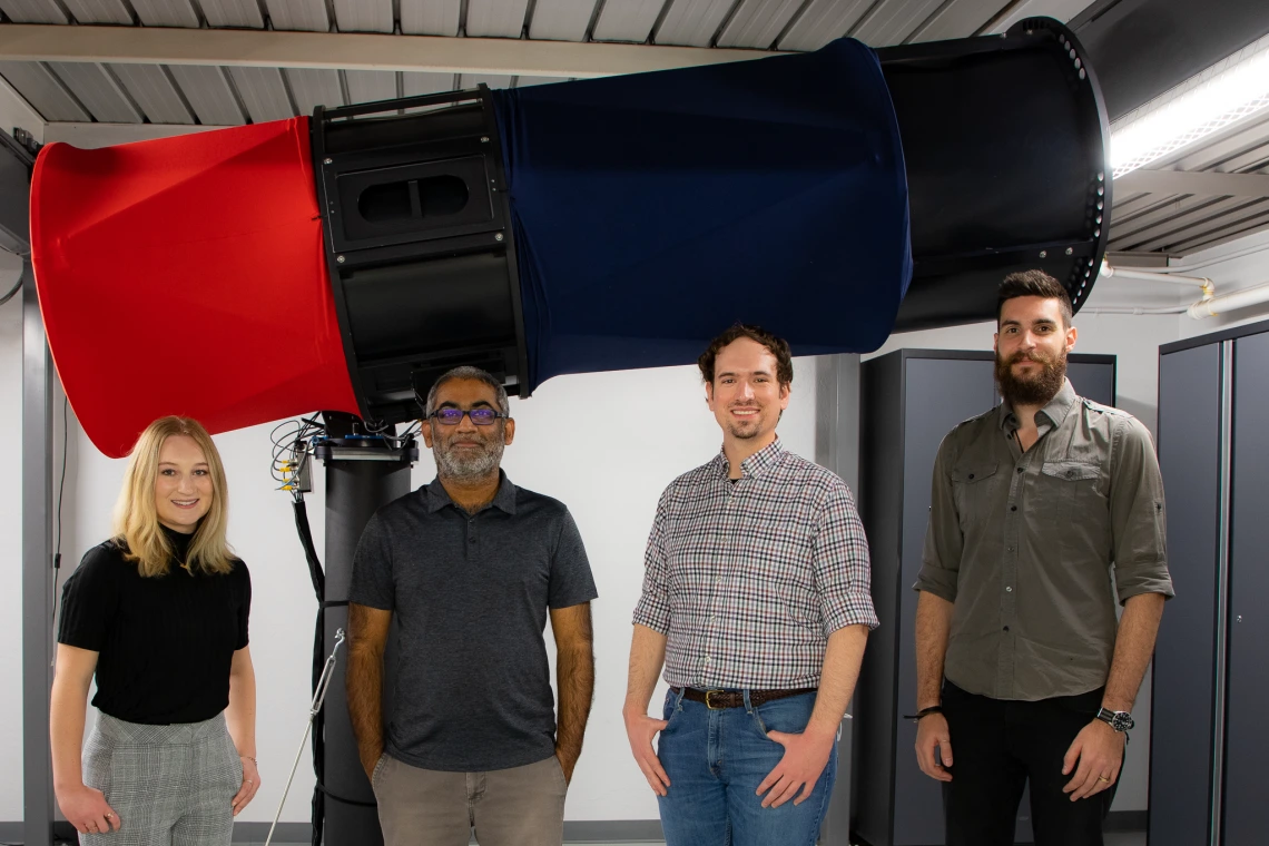 Four people stand in front of a large red and blue telescope.