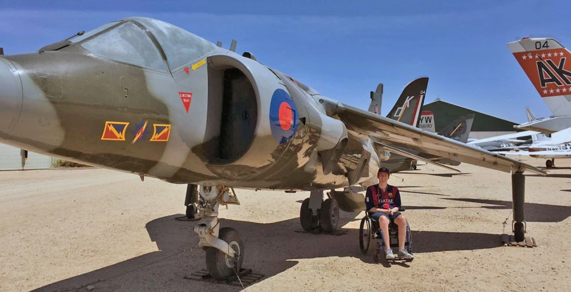 Alex Spartz, an engineering student and wheelchair user, sits in front of an airplane at the Pima Air and Space Museum.