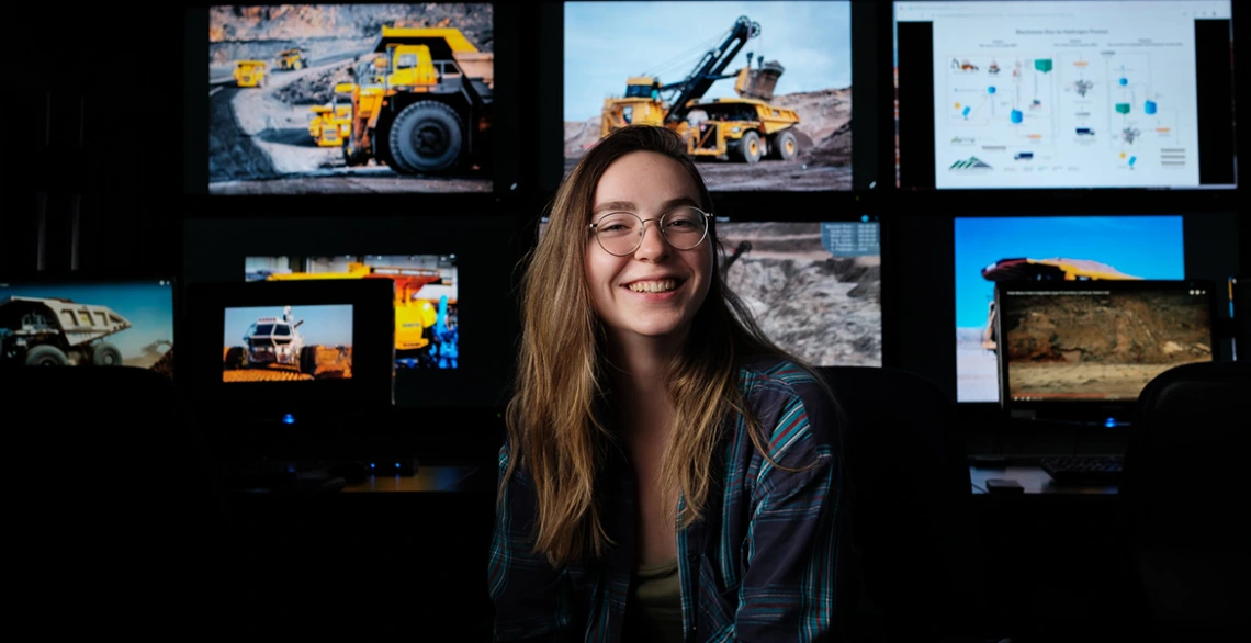 a student poses in front of several screens running mining software