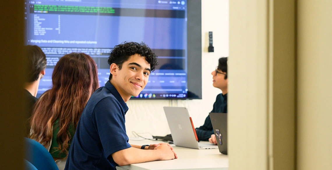 a group of students in a classroom looking at a large monitor