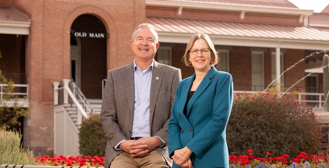 Two people sit in front of the Old Main building on the UA campus