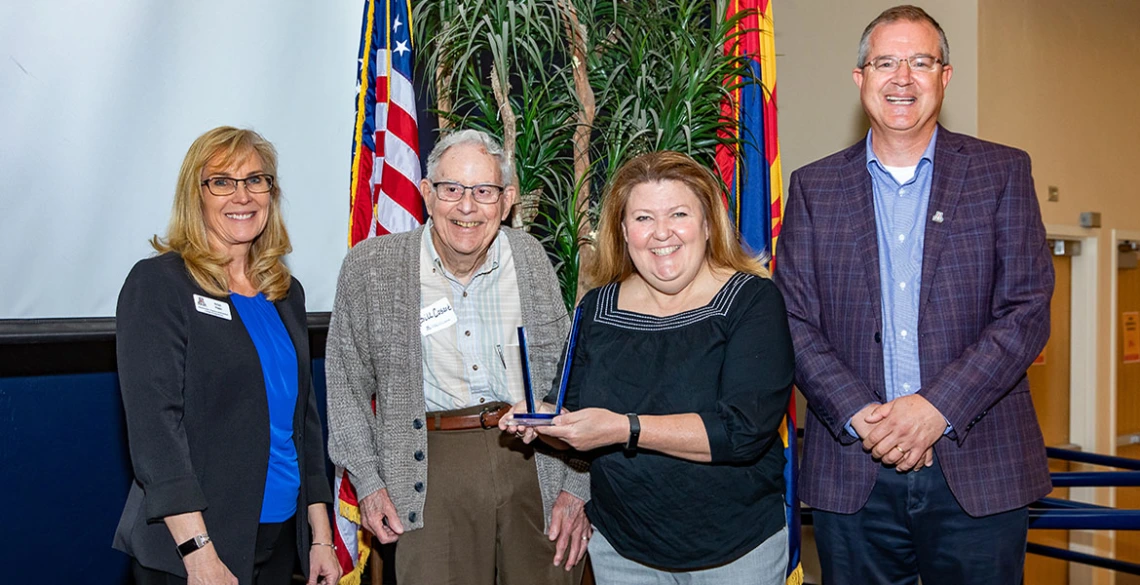 An employee poses for an award with three presenters