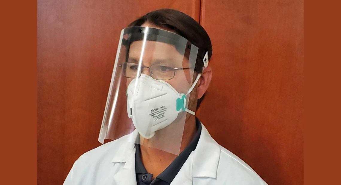 Man wearing a plastic face shield and a white lab coat