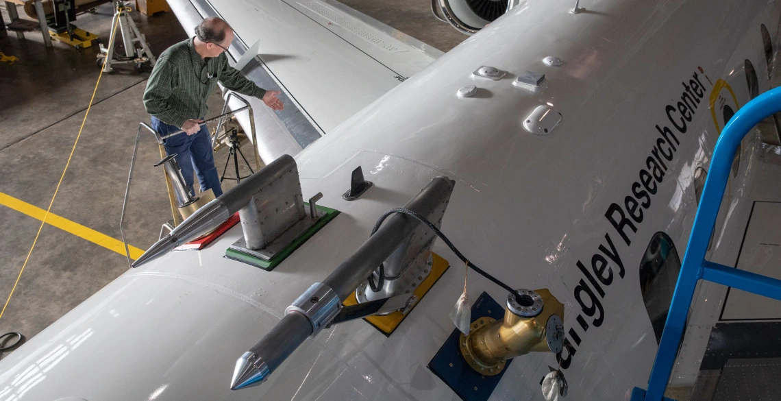 A photo shot from above of a man at the top of a ladder next to a large white airplane, which says "Langley Research Center" on the side.