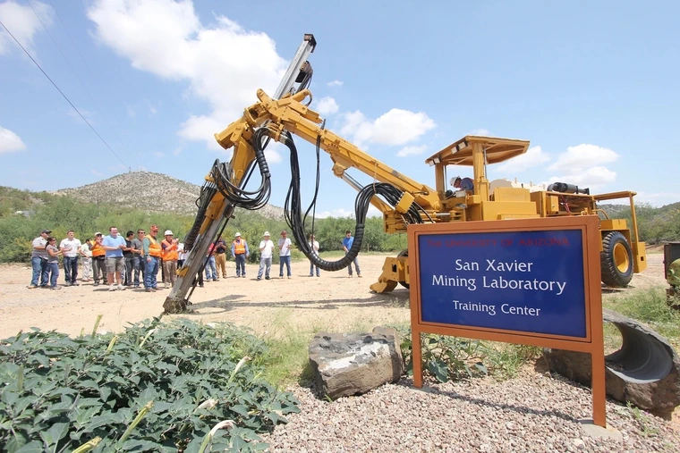 A yellow mining shovel vehicle sits behind a blue sign.