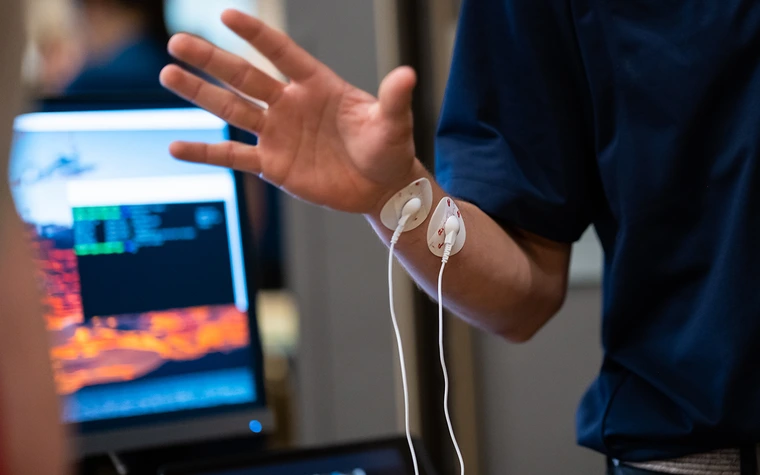 A man in a blue polo demonstrates a medical device on his wrist.
