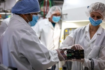 The people in white lab coats handle a small box.